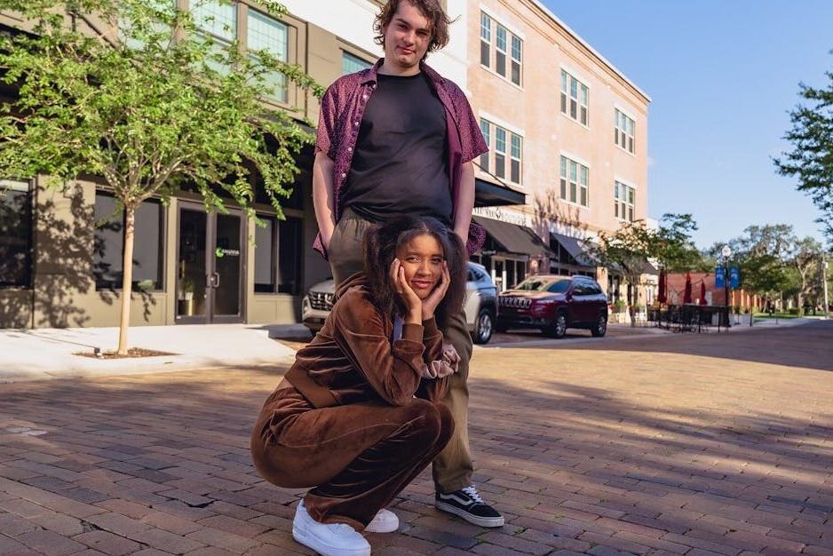 Young adults posing casually on a sunny urban street with a modern backdrop.