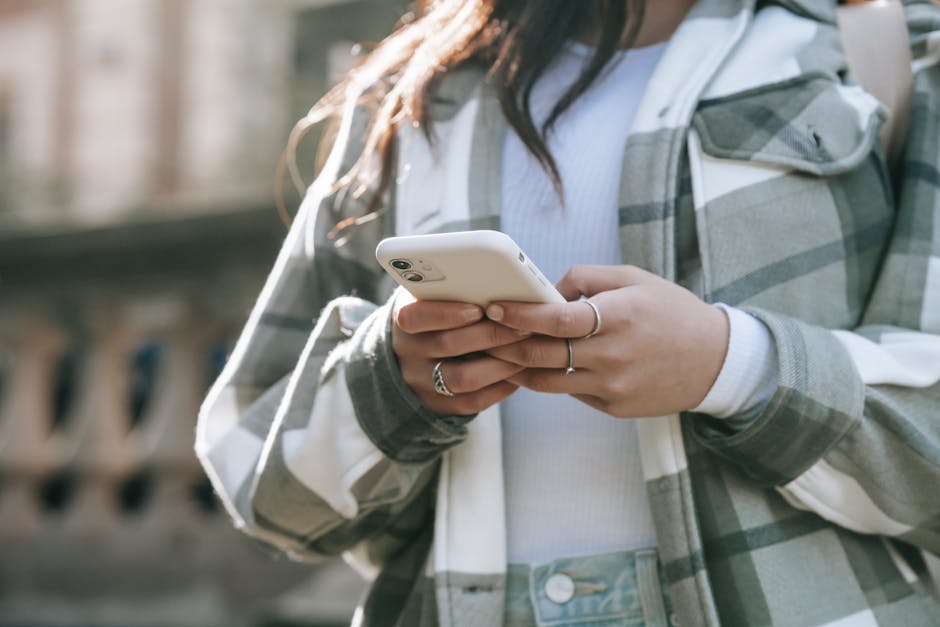 Close-up of a young woman using a smartphone outdoors, wearing a plaid jacket.