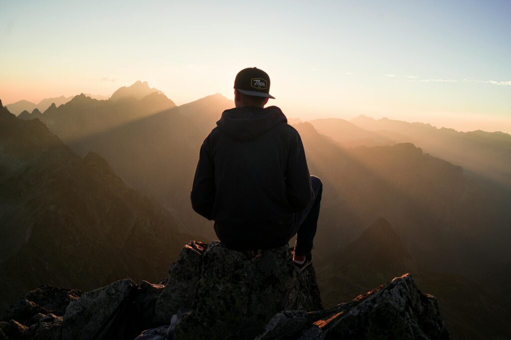 A man sits on a peak in the High Tatras, Slovakia, enjoying a serene sunset view over the mountains.